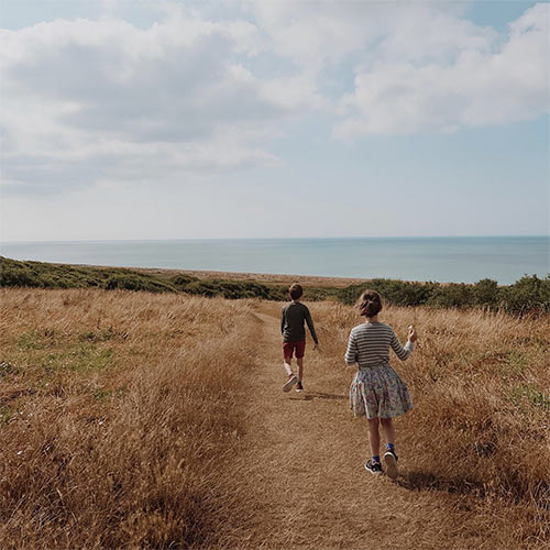 two kids running in the dunes with sea in the background