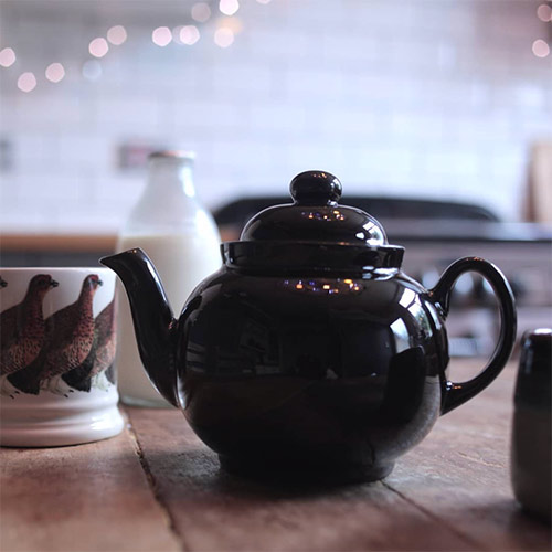 a teapot, mugs and milk on a kitchen table