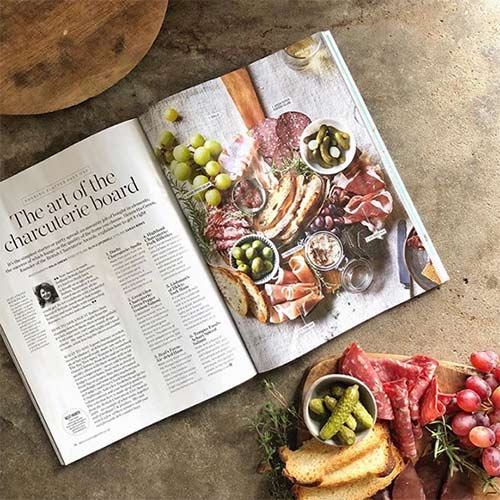 a flat lay with a magazine and some salami and crackers on a board