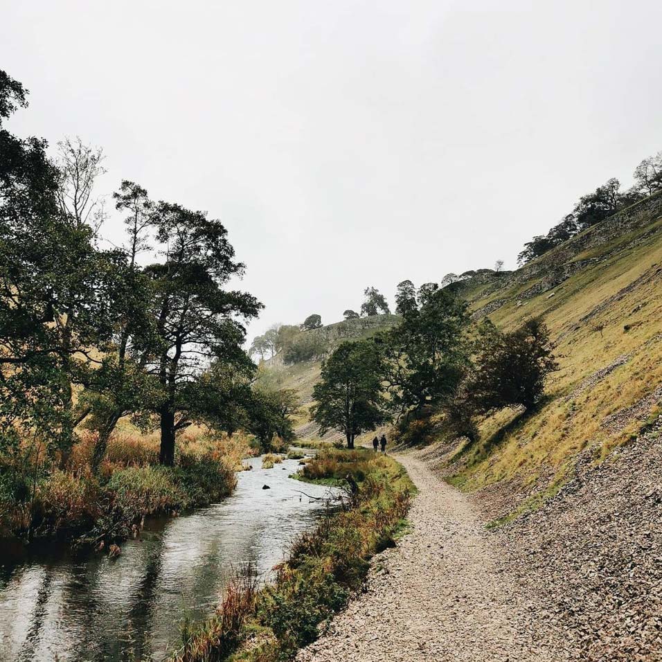 countryside view with a path alongside a river with trees and two people walking