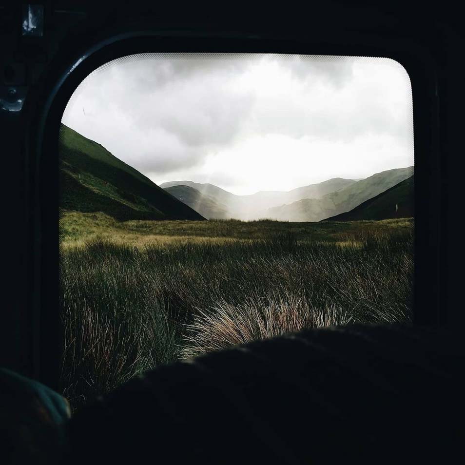 sun rays shining through the clouds seen from behind a car window that frames the view