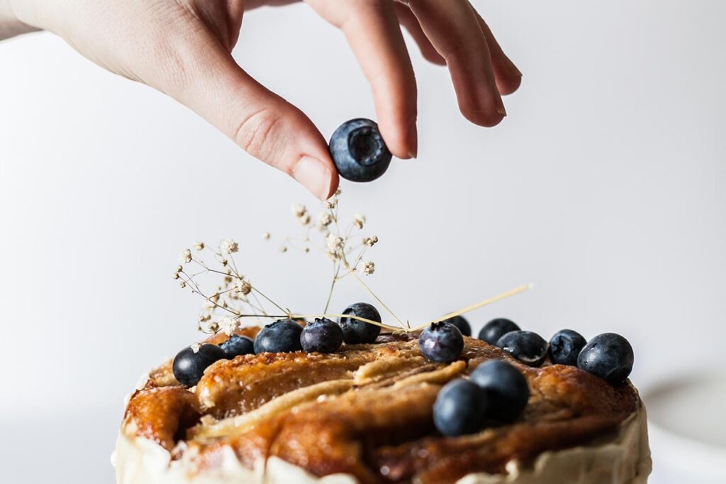 a woman's hand putting a blueberry on top of a cake