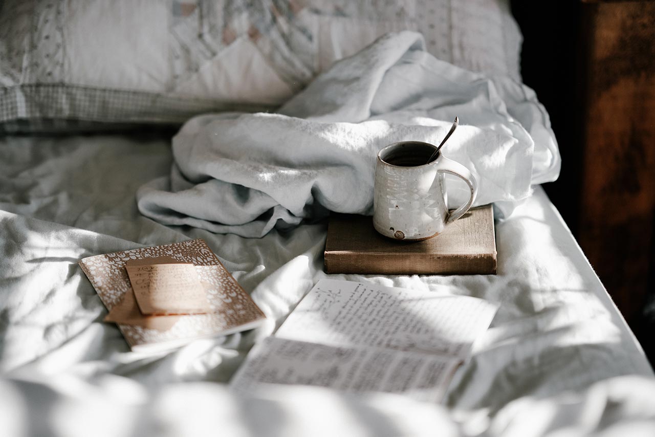 a bed with several journals, a book and a cup of tea