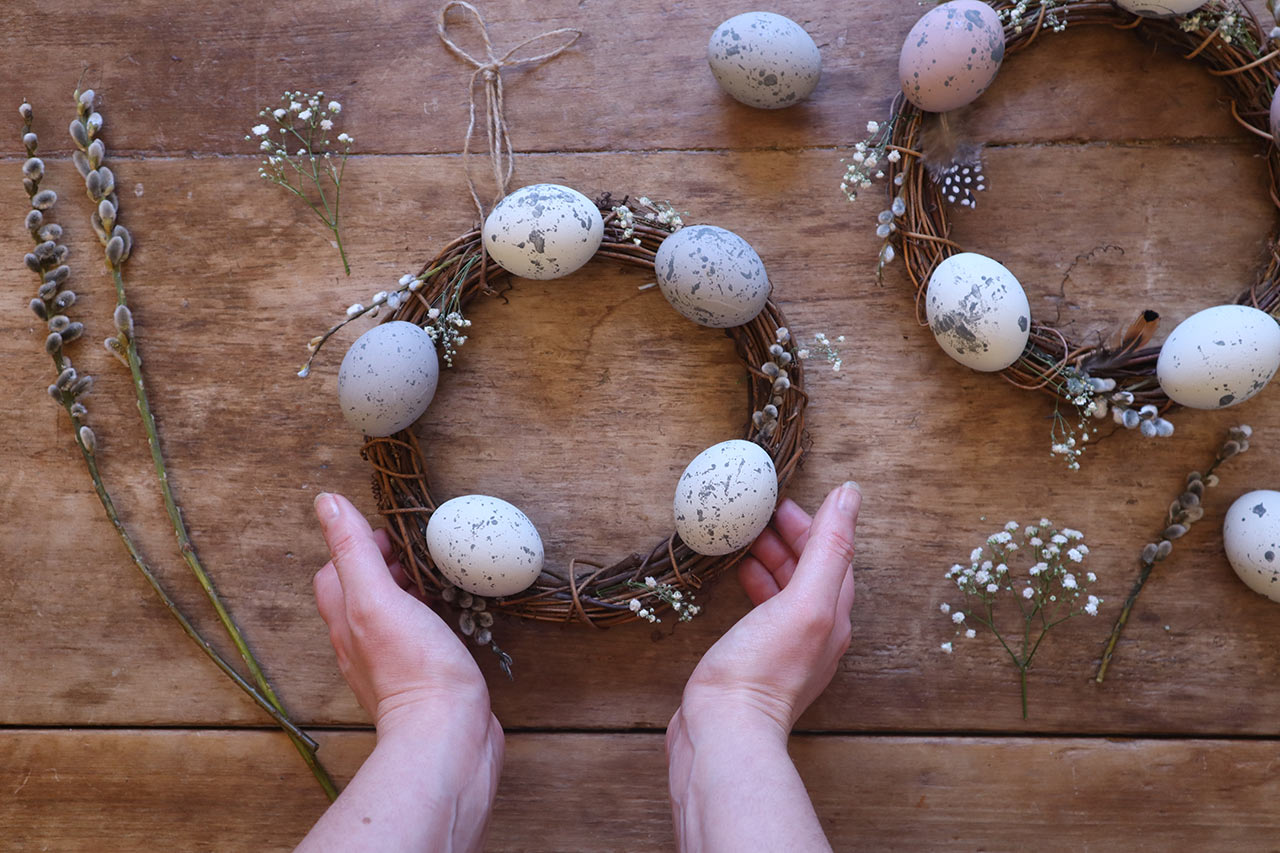 two hands holding a spring wreath with twigs, flowers and eggs - a spring guide to hygge