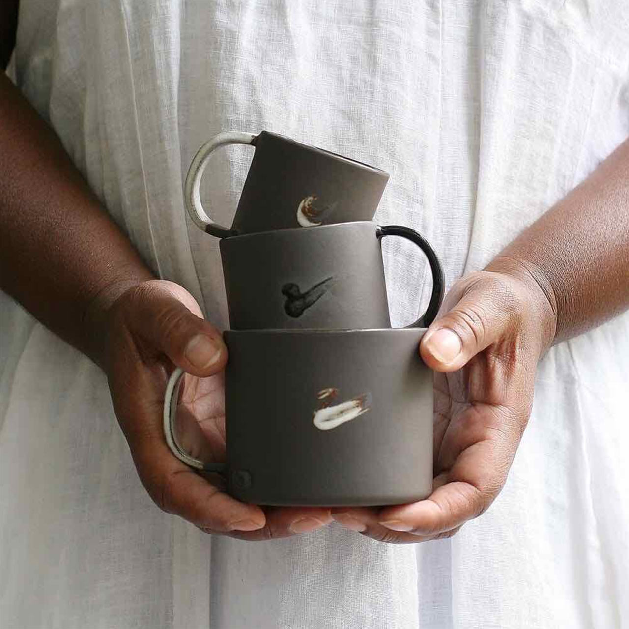 two hands holding 3 different sizes of mugs from naked clay ceramics