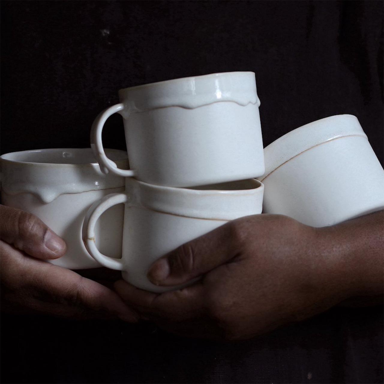 two hands holding 4 white ceramic mugs from naked clay ceramics