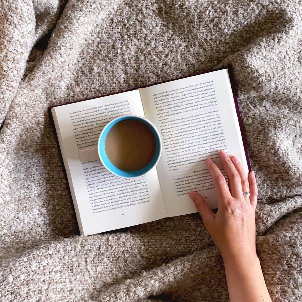 a blanket with a book and a cup of coffee with a hand on the book seen from above, slow morning ritual, business boundaries