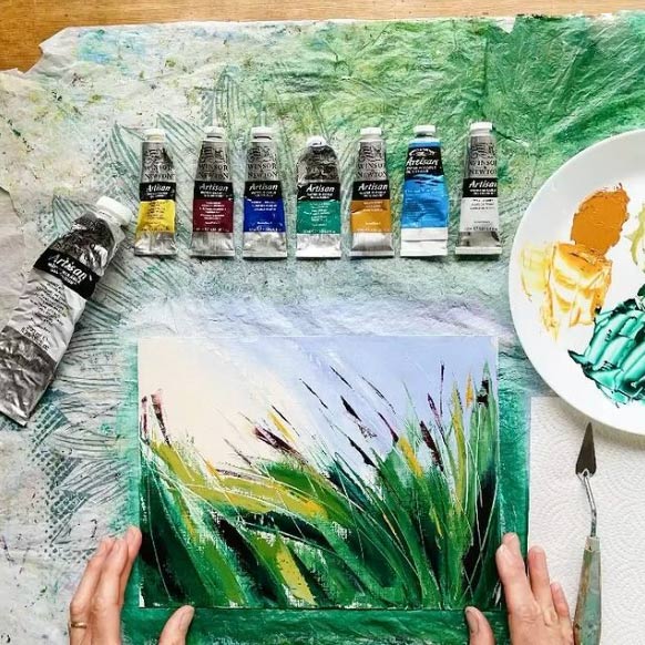 flatlay of a small nature-inspired painting with tubes of paint and a mixing plate laying next to it