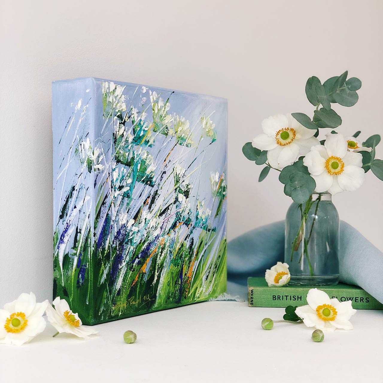 small floral painting standing against a wall, a vase with flowers next to it and a copy of British wildflowers