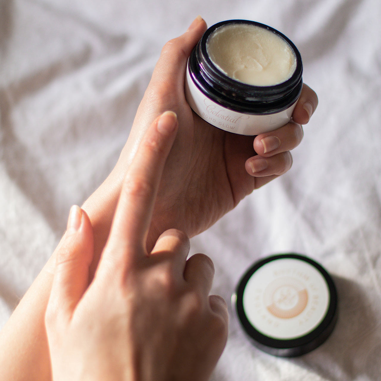 a woman's hand holding a small jar of balm