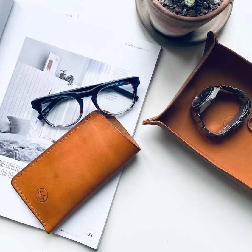 flatlay of a magazine, glasses case and basket in brown leather