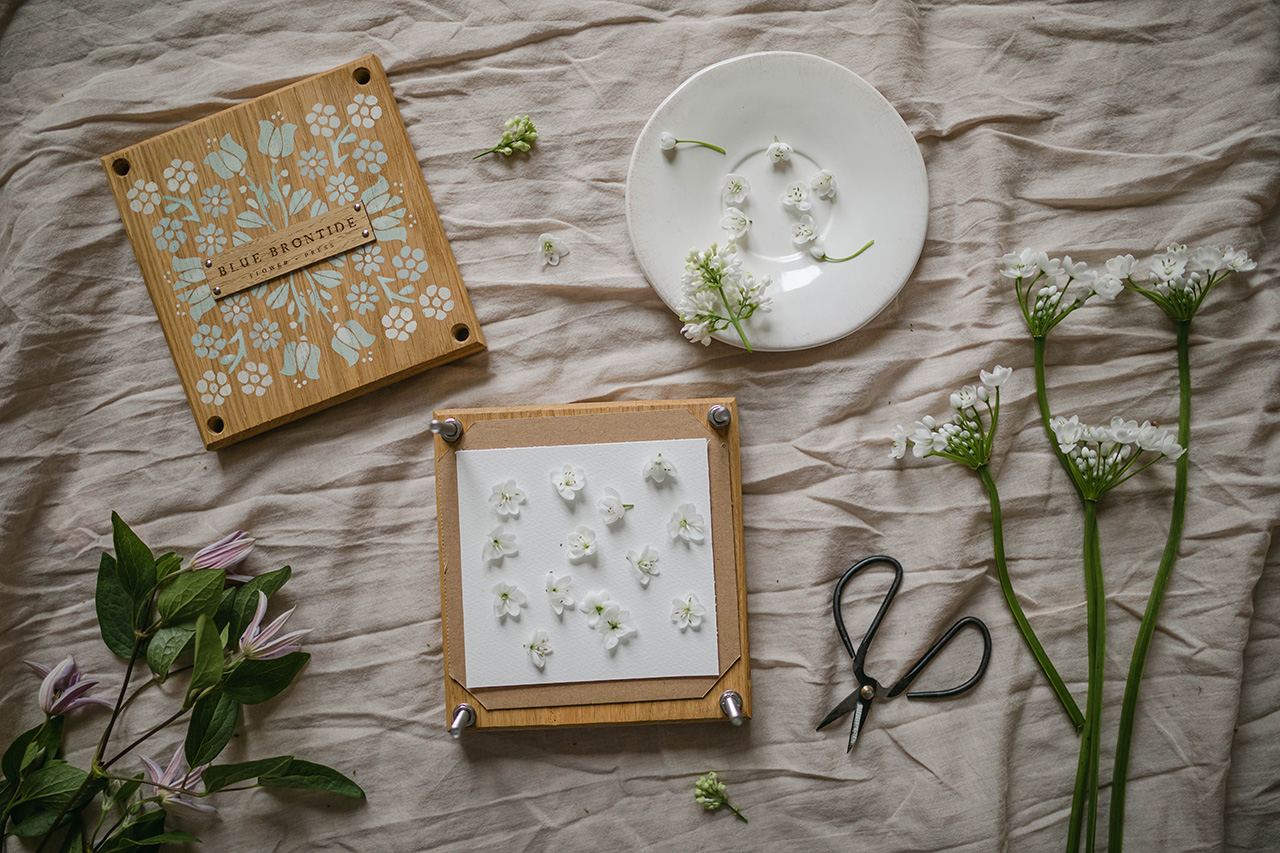 flatlay of a flower press, flowers and scissors on a linen cloth