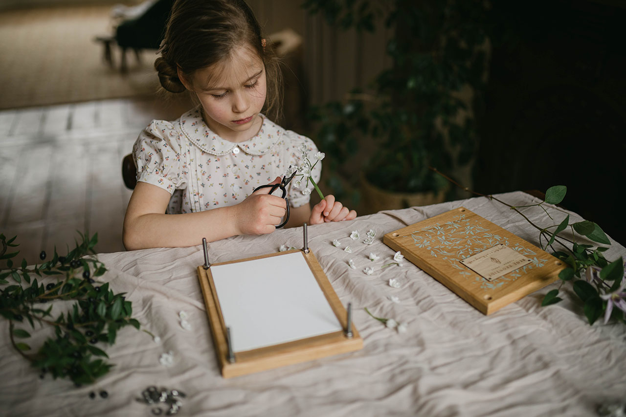 a girl sitting at a table with a flower press