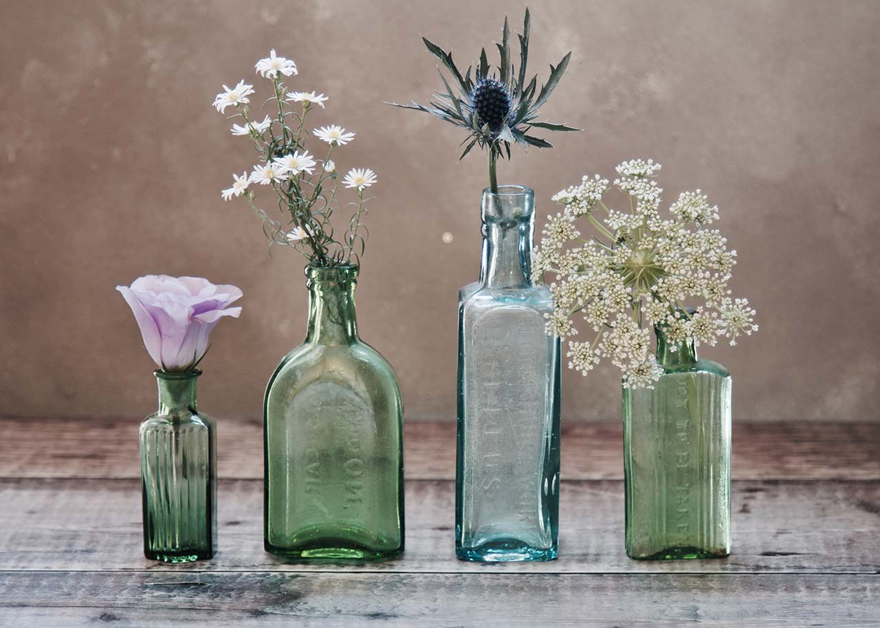 slow living in spring - four pastel coloured glass vases with single stem flower in them