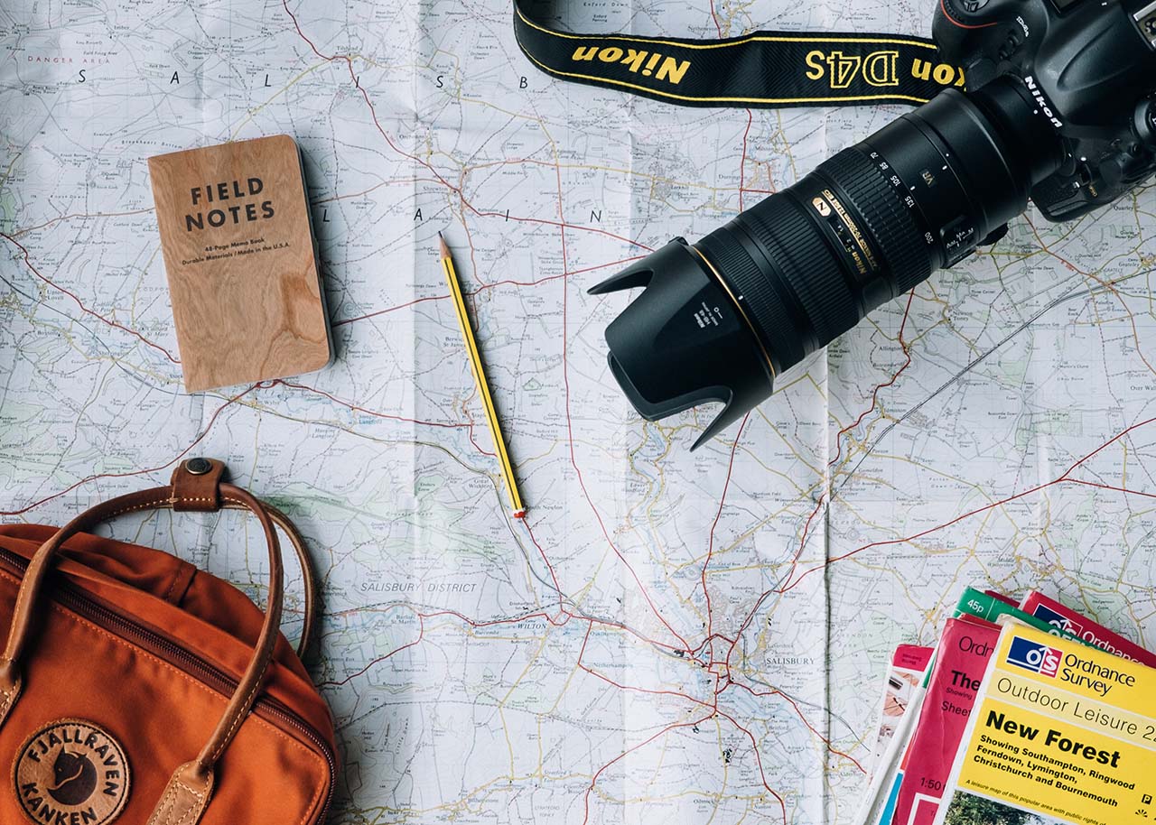 a map with a notebook, pencil, backpack and a camera - why slow travel is the perfect way to enjoy summer