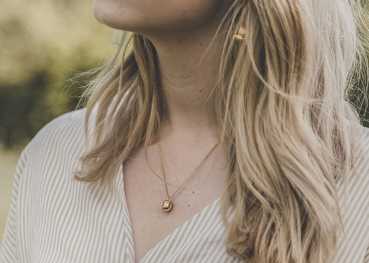autumn jewellery - woman wearing a gold necklace with a tiny golden acorn pendant