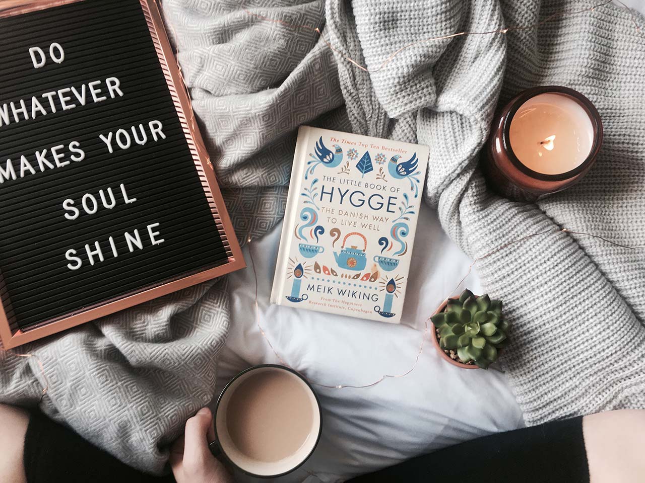 flatlay on a bed with a candle, a book, a cup of coffee and a text board reading do whatever makes your soul shine