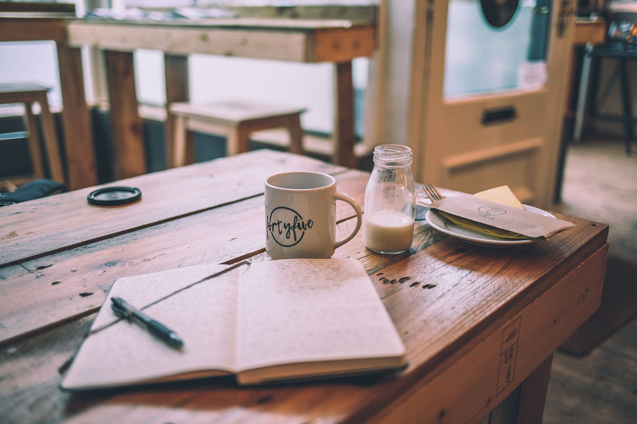 a table with an open journal and a pen and a cup of coffee