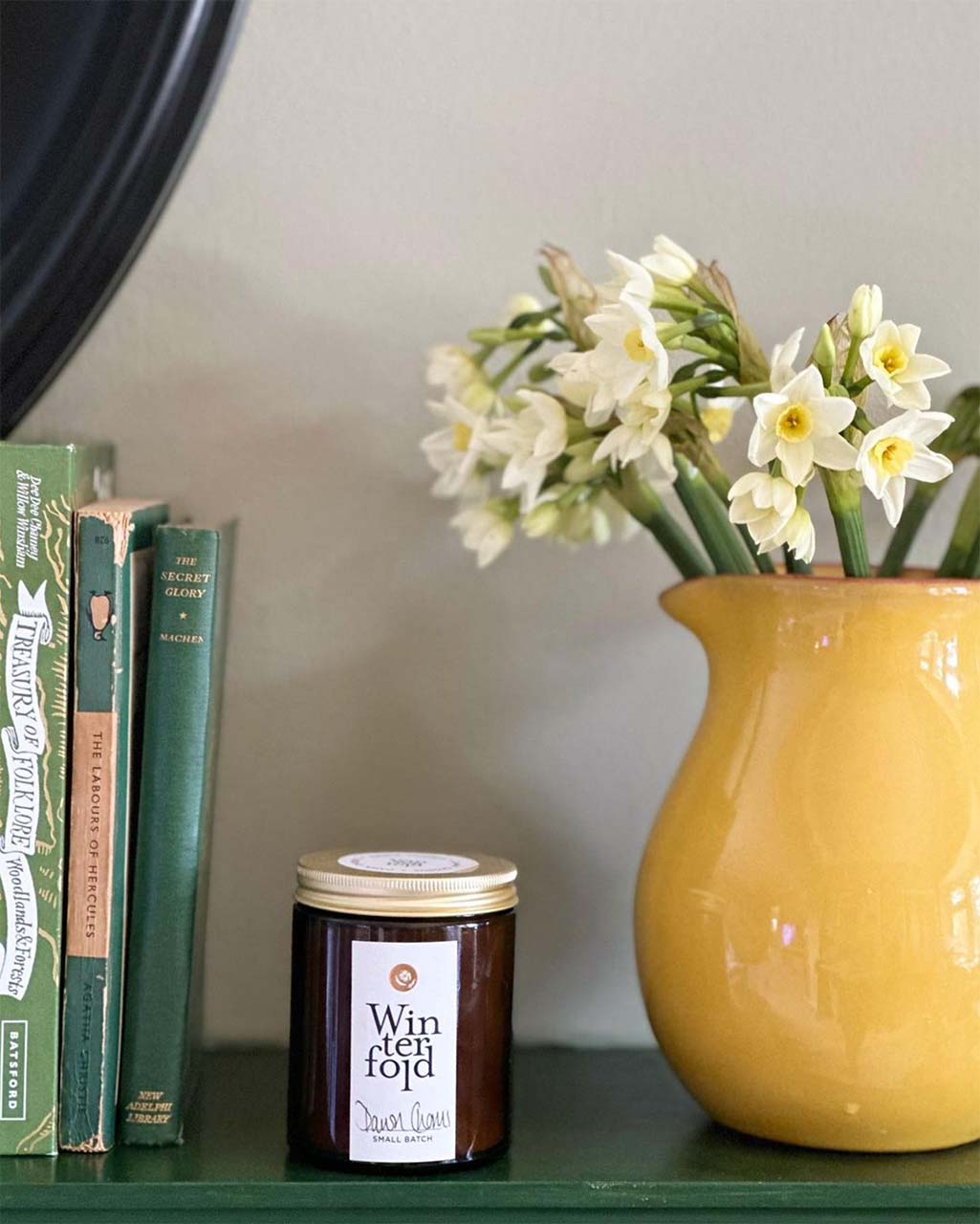 a spring candle with a yellow vase with daffodils and a few green books - everyday spring ritual