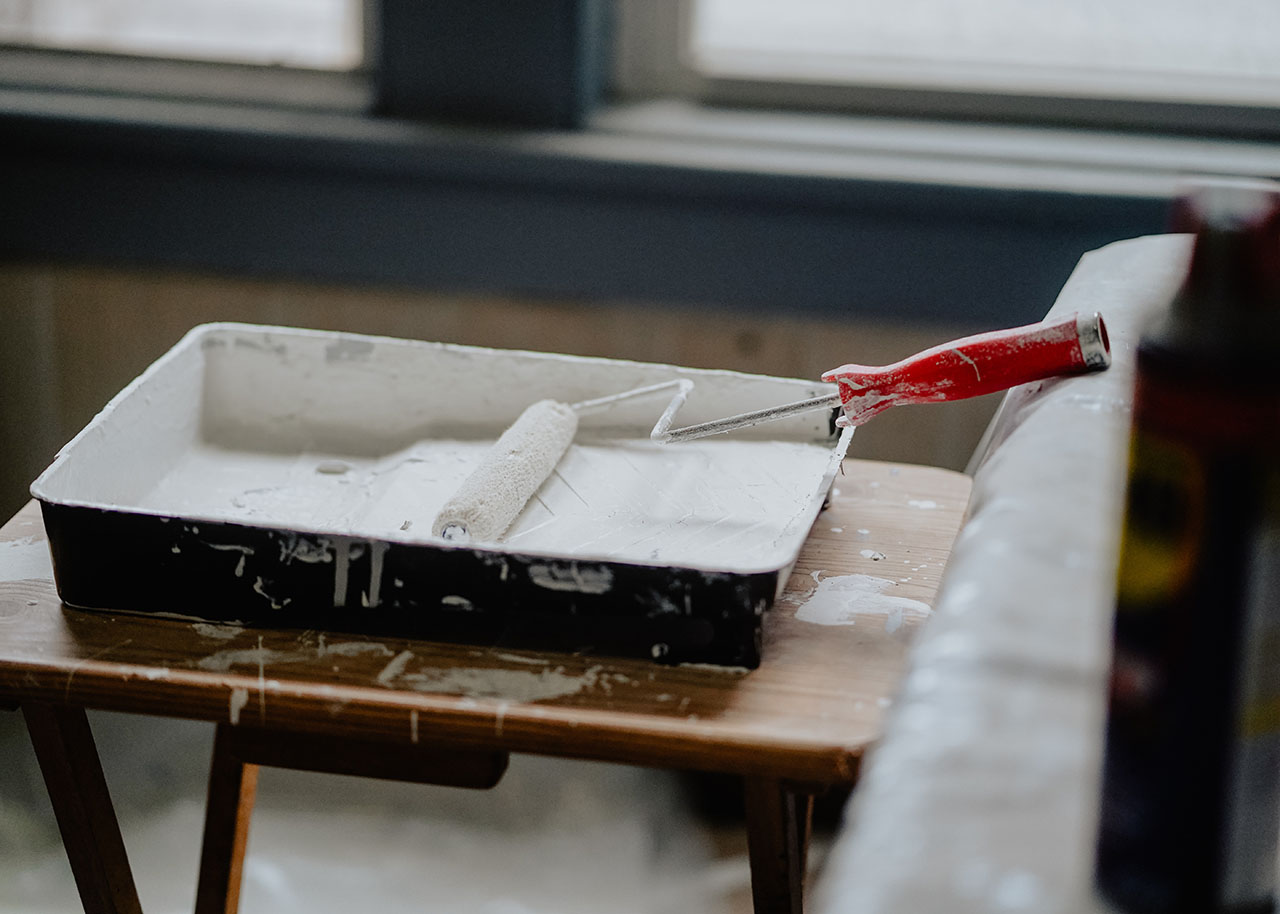 a tray with white paint and a paint roller on a wooden table