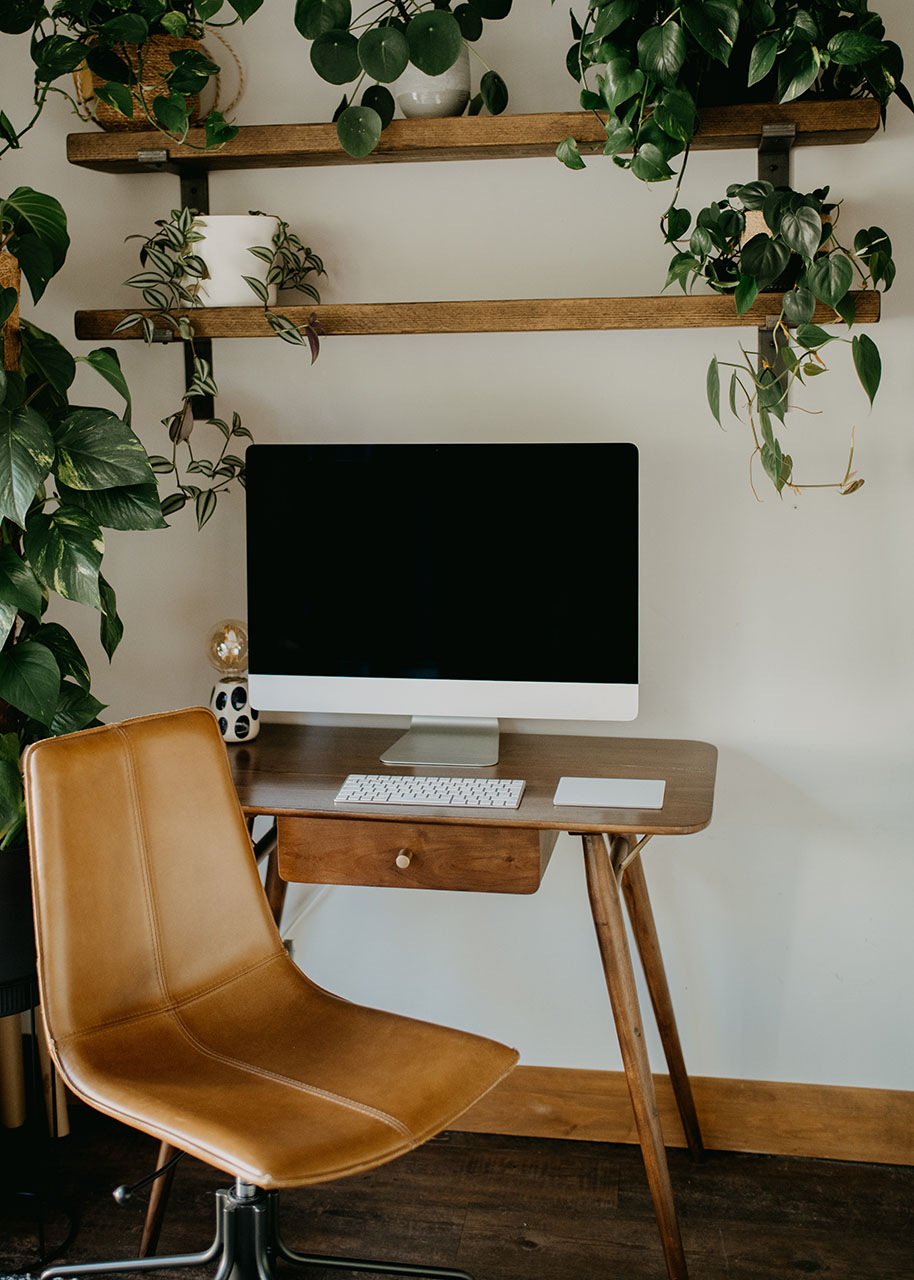 cosy home office set up with a computer on a small desk, a leather chair and shelves with plants - simplifying tasks