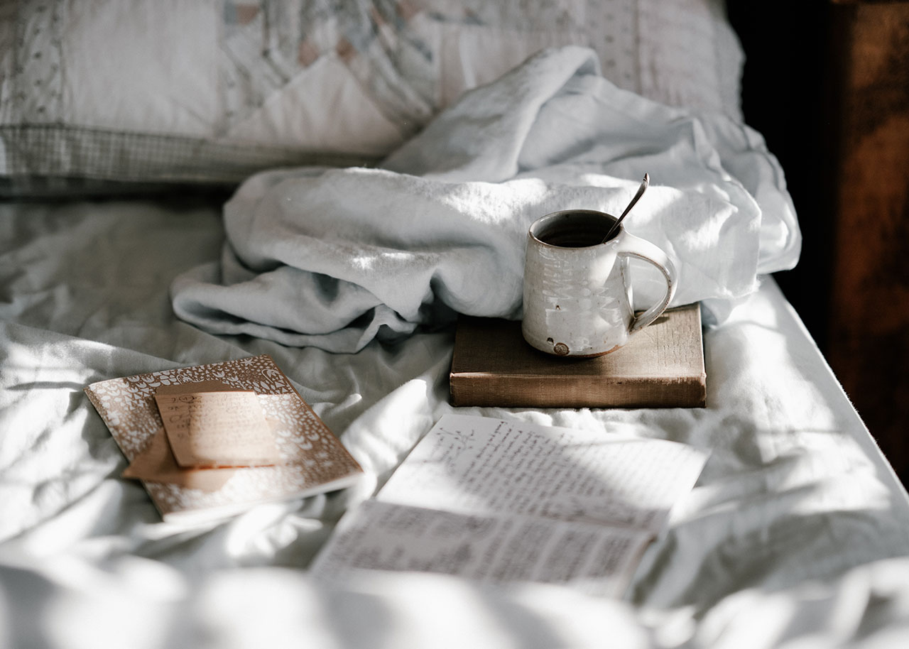 a bed with a book, notes and a cup of tea - your slow living reading list