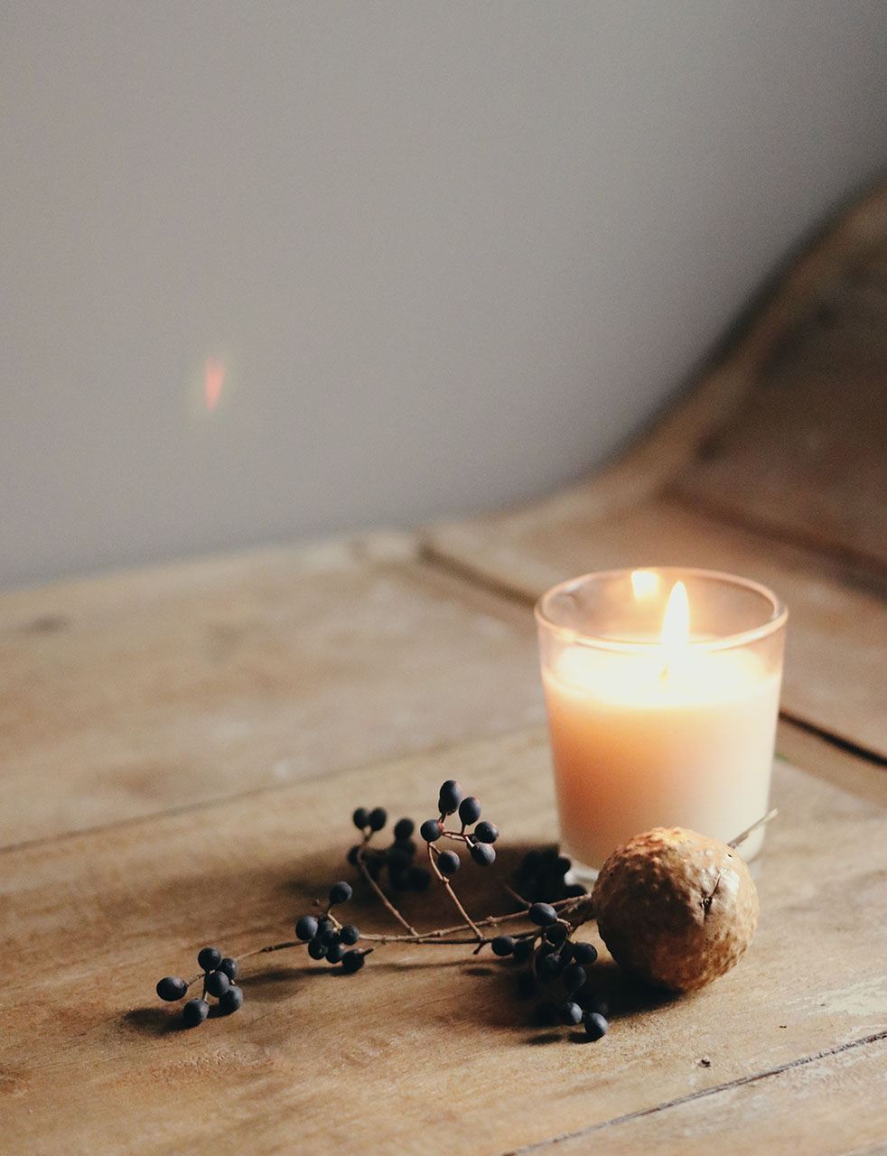 Candle in a glass on a wooden floor with seasonal decoration next to it