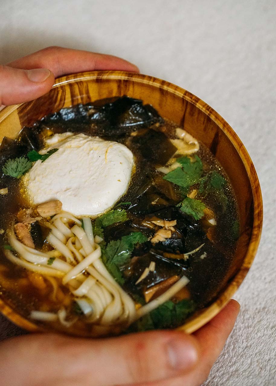 two hands holding a wooden bowl with miso soup