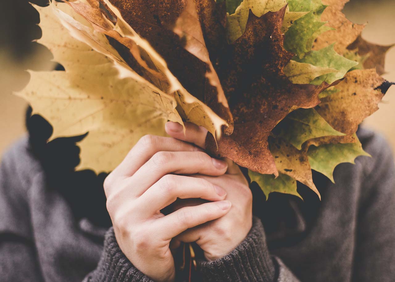 a woman hiding behind a handful of autumn leaves - autumn rituals