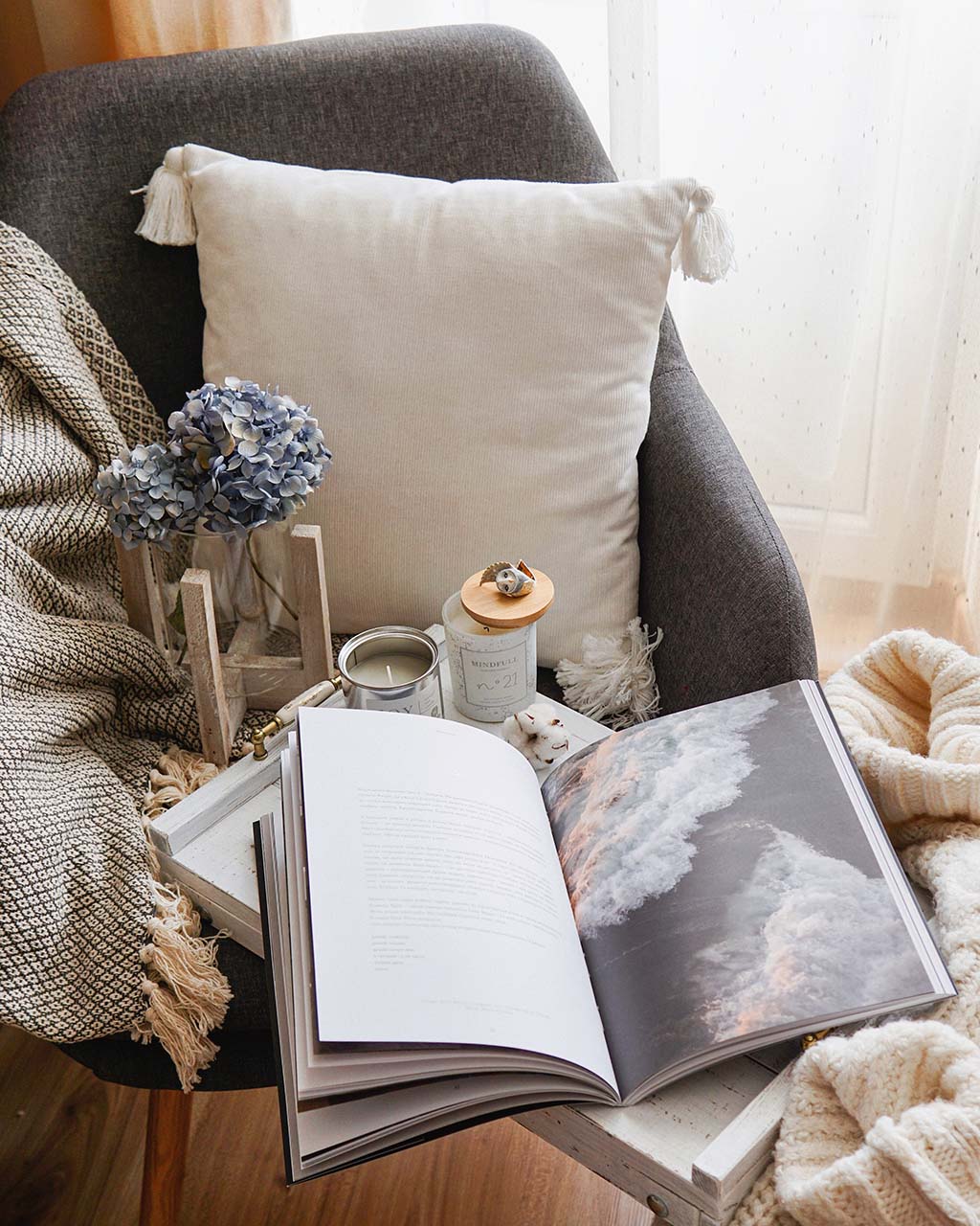 cosy reading nook with comfy blankets, cushions, a book, a candle