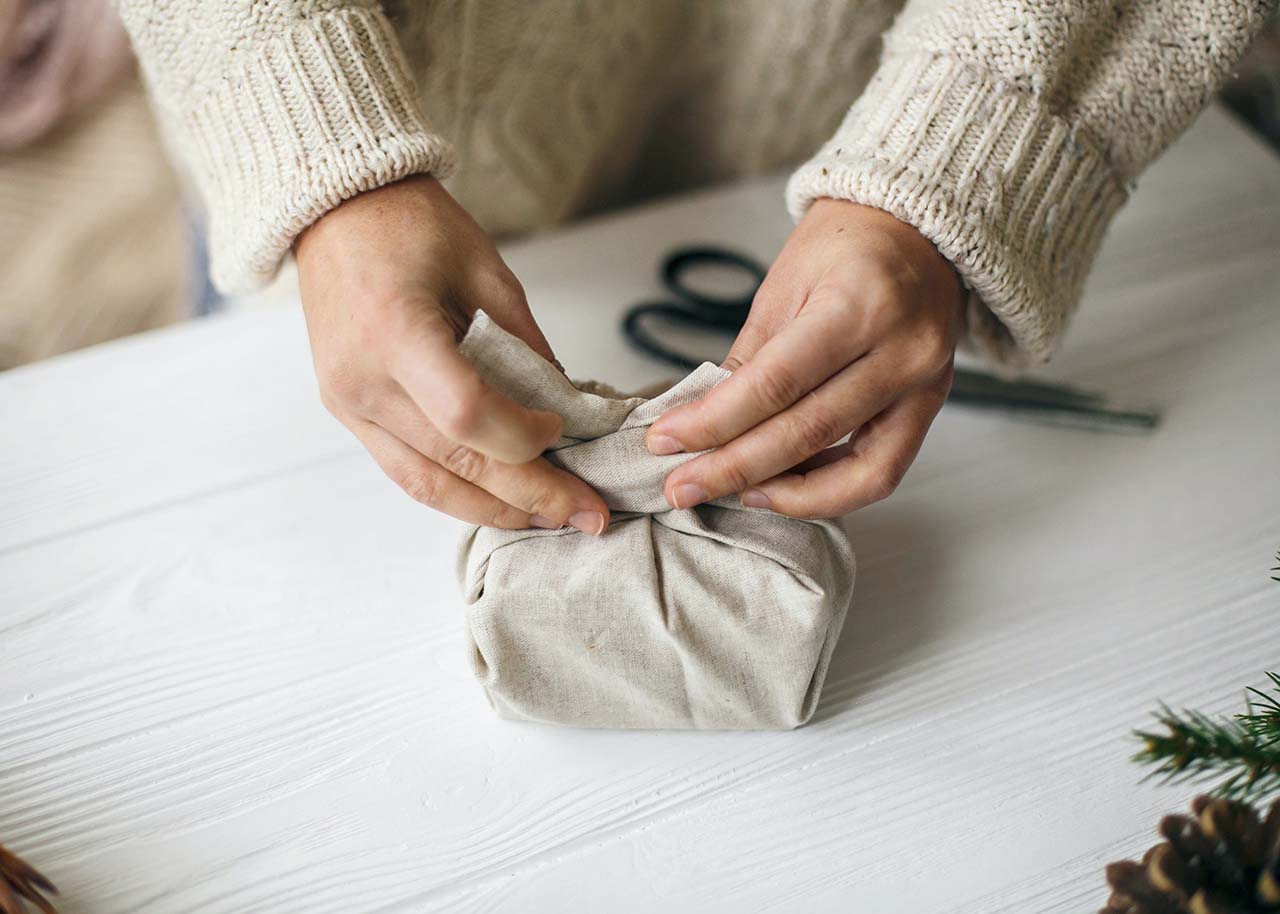a woman wrapping a gift with a piece of cloth - sustainable gift giving