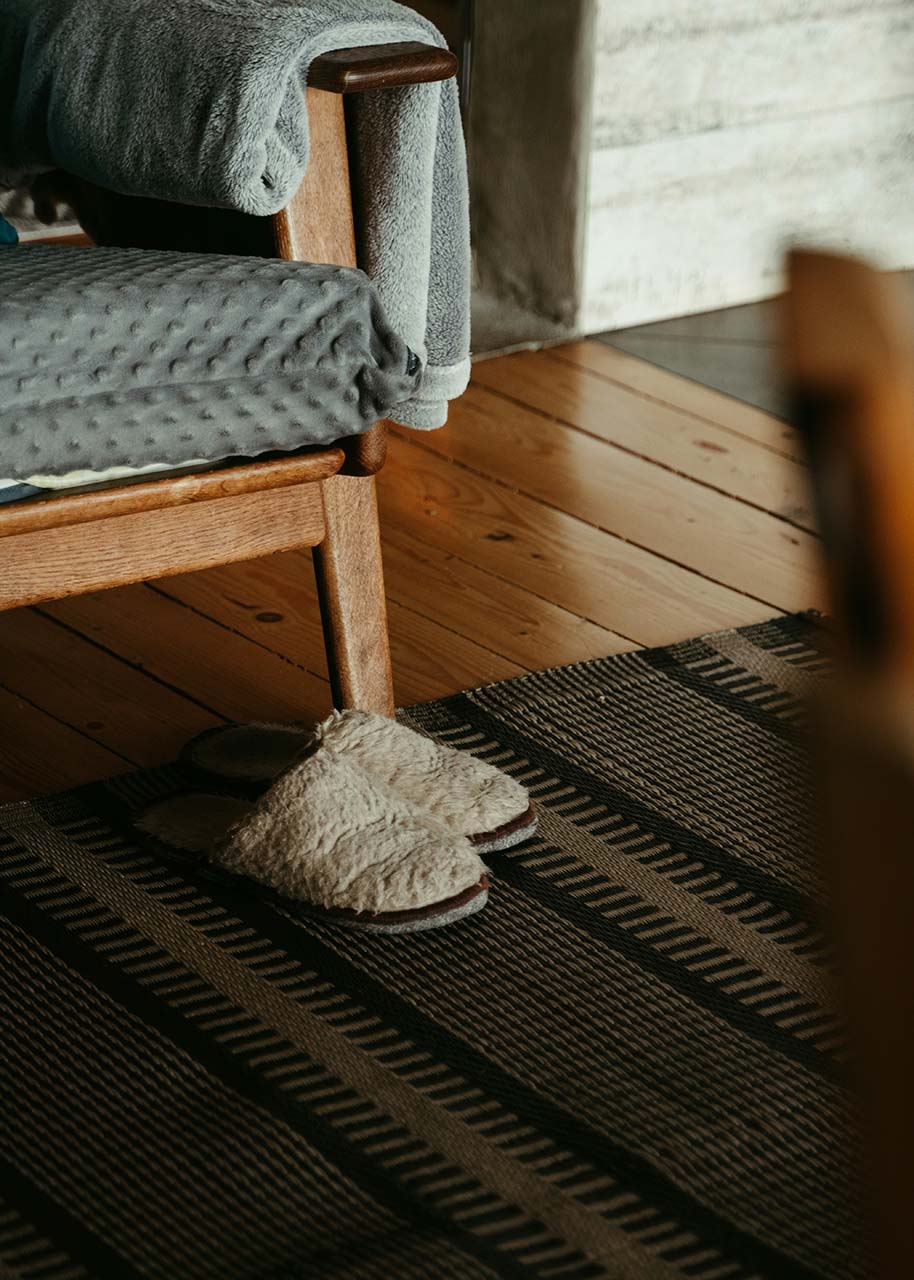 an armchair with a blanket on a carpet with slippers next to it - cosy home