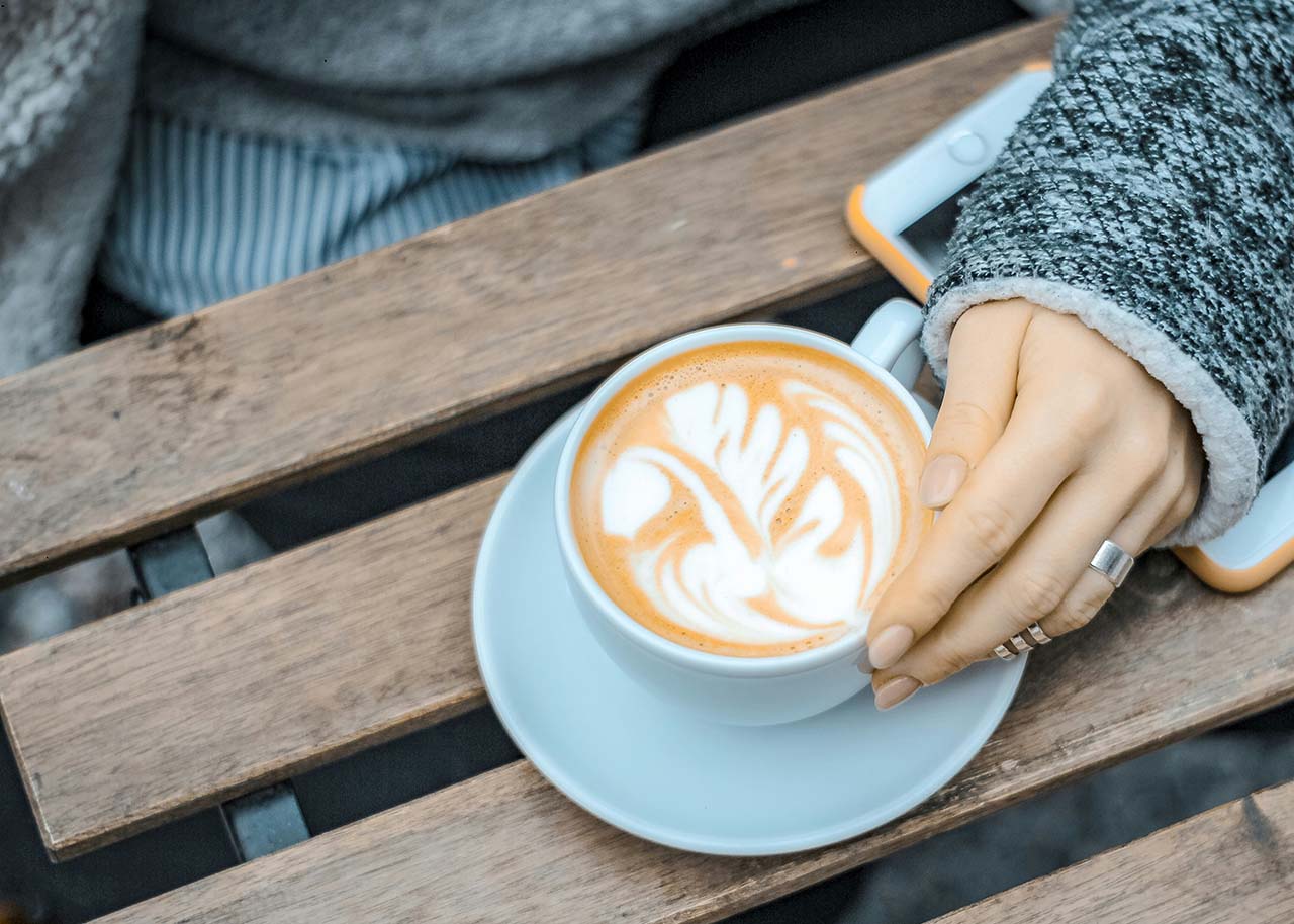 Mindful tech use - a woman's hand holding a cup of coffee with her arm covering a phone